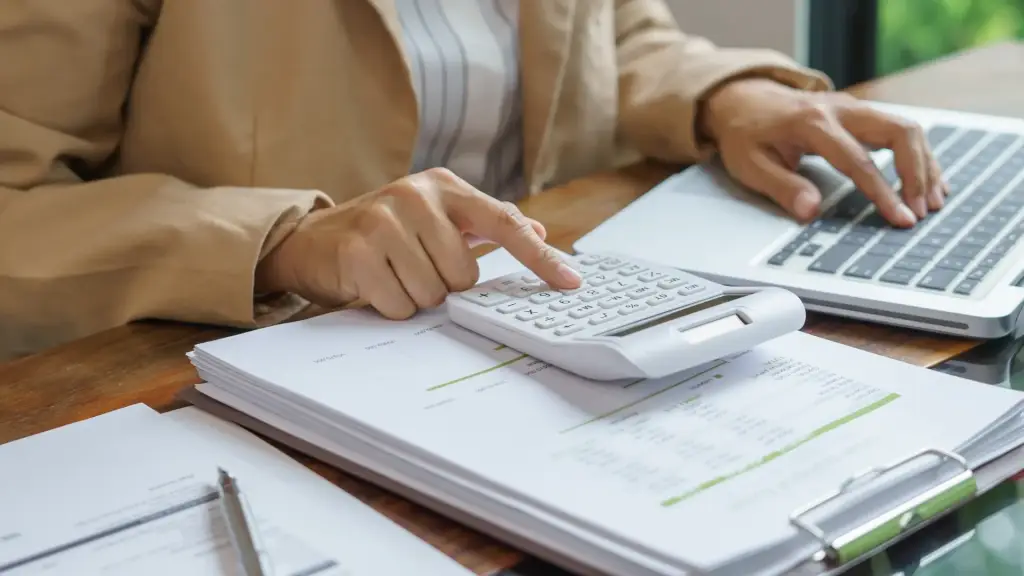 A woman sitting at a desk with their calculator and laptop, working on taxes.
