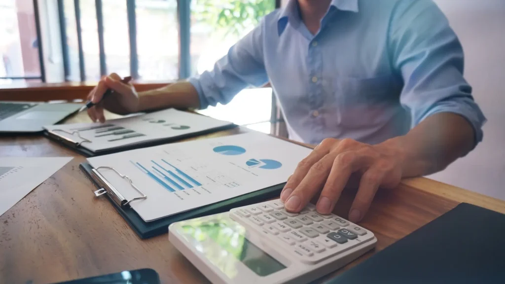 A financial professional reviews bar charts and pie charts on a clipboard while using a calculator, representing outsourced CFO services and small business financial planning.