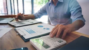 A financial professional reviews bar charts and pie charts on a clipboard while using a calculator, representing outsourced CFO services and small business financial planning.