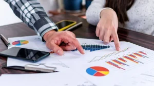 Two business professionals review financial charts and KPI reports spread across a table, representing scalable financial planning and outsourced CFO strategy for growing companies.